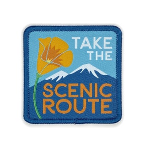 May include: A blue and orange embroidered patch with a poppy flower and mountains. The text on the patch reads "Take the Scenic Route."