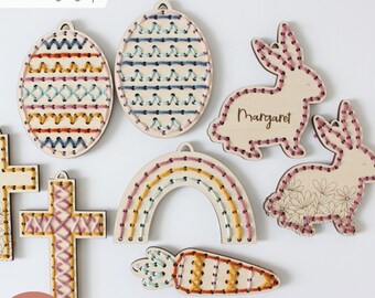 Pode incluir: Um conjunto de ornamentos de Páscoa de madeira cortados a laser para costura com fio. O conjunto inclui uma cruz, um arco-íris, uma cenoura, dois ovos e dois coelhos. Um coelho tem o nome "Margaret" escrito nele.