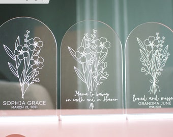 May include: Three white acrylic arch-shaped signs with forget-me-not flowers and personalized text. The signs read "Mama to babies on earth and in Heaven", "Sophia Grace March 21, 2021", and "Loved and missed Grandma June 1958-2023".