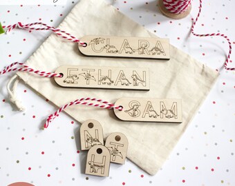 May include: Set of wooden gift tags with dinosaur illustrations and names Clara, Ethan, and Sam.  The tags are on a white background with red and white polka dots.  There are also three smaller wooden tags with the letters N, T, and H.