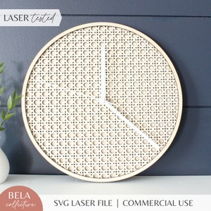 Puede incluir: Una esfera de reloj blanca con un patrón de caña tejido sobre un fondo de madera clara. Las manecillas del reloj son blancas y el reloj está cortado con láser. El texto "LASER tested" es visible en la esquina superior izquierda de la imagen.