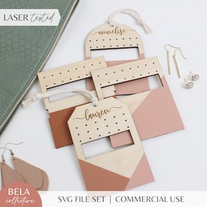 Peut inclure: Trois supports à boucles d'oreilles en bois avec des motifs géométriques dans des tons de rose et de brun. Chaque support a une découpe pour les boucles d'oreilles et un espace pour un nom. Les noms sont "Annelise", "Lauren" et un troisième nom qui n'est pas visible sur l'image. Les supports sont découpés au laser et ont une boucle en corde pour la suspension.