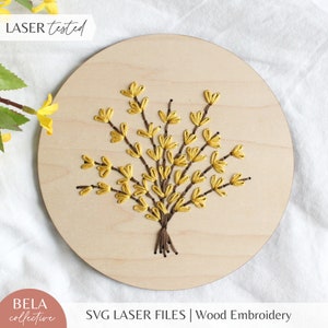 Könnte beinhalten: Eine runde Holzplakette mit einem gelben gestickten Blumenmuster. Das Muster zeigt eine Ansammlung gelber Blumen mit braunen Stielen. Die Plakette trägt den Text "LASER tested" oben links und "SVG LASER FILES | Wood Embroidery" unten rechts.