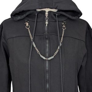 K&ouml;nnte beinhalten: Ein schwarzer Kapuzenpullover mit Rei&szlig;verschluss und langen Kordelz&uuml;gen an der Kapuze. Die Kordelz&uuml;ge enden in silberfarbenen Metallenden. Eine silberfarbene Metallkette mit dekorativen zylindrischen Perlen verbindet die Kordeln.