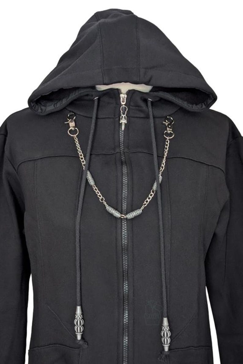 K&ouml;nnte beinhalten: Ein schwarzer Kapuzenpullover mit Rei&szlig;verschluss und langen Kordelz&uuml;gen an der Kapuze. Die Kordelz&uuml;ge enden in silberfarbenen Metallenden. Eine silberfarbene Metallkette mit dekorativen zylindrischen Perlen verbindet die Kordeln.