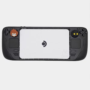 May include: Black Steam Deck console with a white center panel and a character design on the left side. The console has buttons and a joystick on both sides. The text "Fits Steam Deck" is at the bottom.