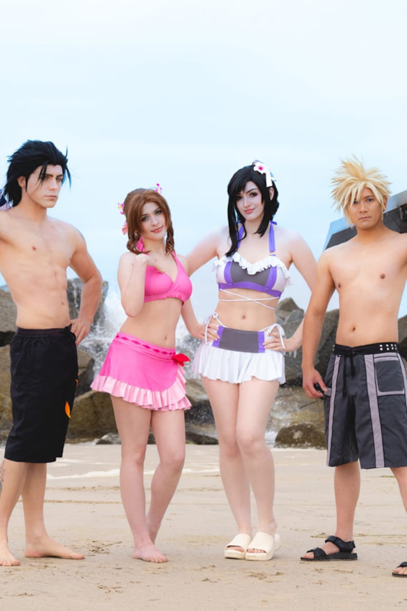 May include: Four people dressed in swimwear on a beach. Two women are wearing bikinis and skirts, one man is wearing black swim trunks, and the other man is wearing black and grey swim trunks.