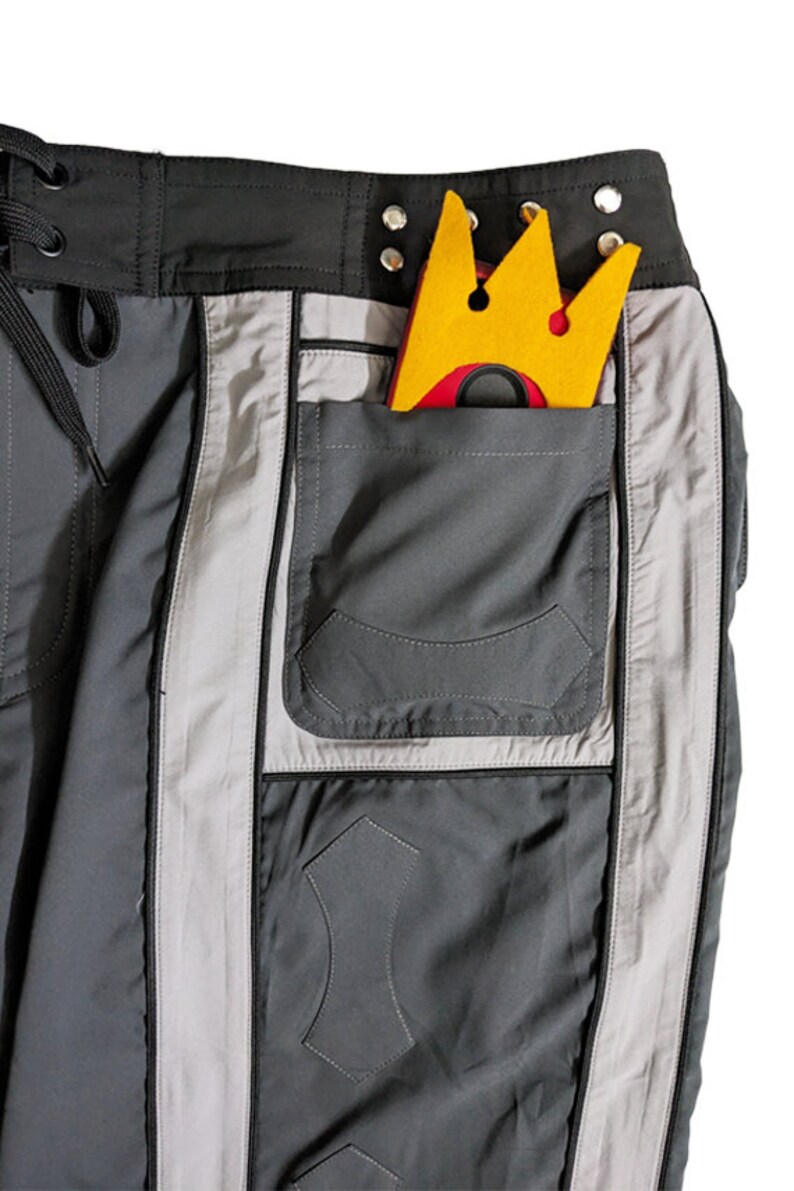 May include: Gray cargo pants with a large pocket on the right side. A yellow crown with a red center is in the pocket.