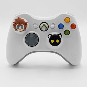May include: White Xbox controller with character art. The controller has a gray directional pad and buttons in various colors. The text "Fits Xbox/360/One/Series" is at the bottom.