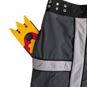 May include: Black cargo pants with a silver reflective stripe down the side. A yellow and red phone case with a crown design is in the front pocket.