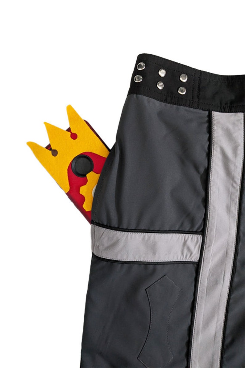 May include: Black cargo pants with a silver reflective stripe down the side. A yellow and red phone case with a crown design is in the front pocket.