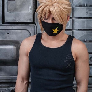 May include: A person wearing a black tank top with a yellow star on a black face mask. The tank top has a white inscription on the front.