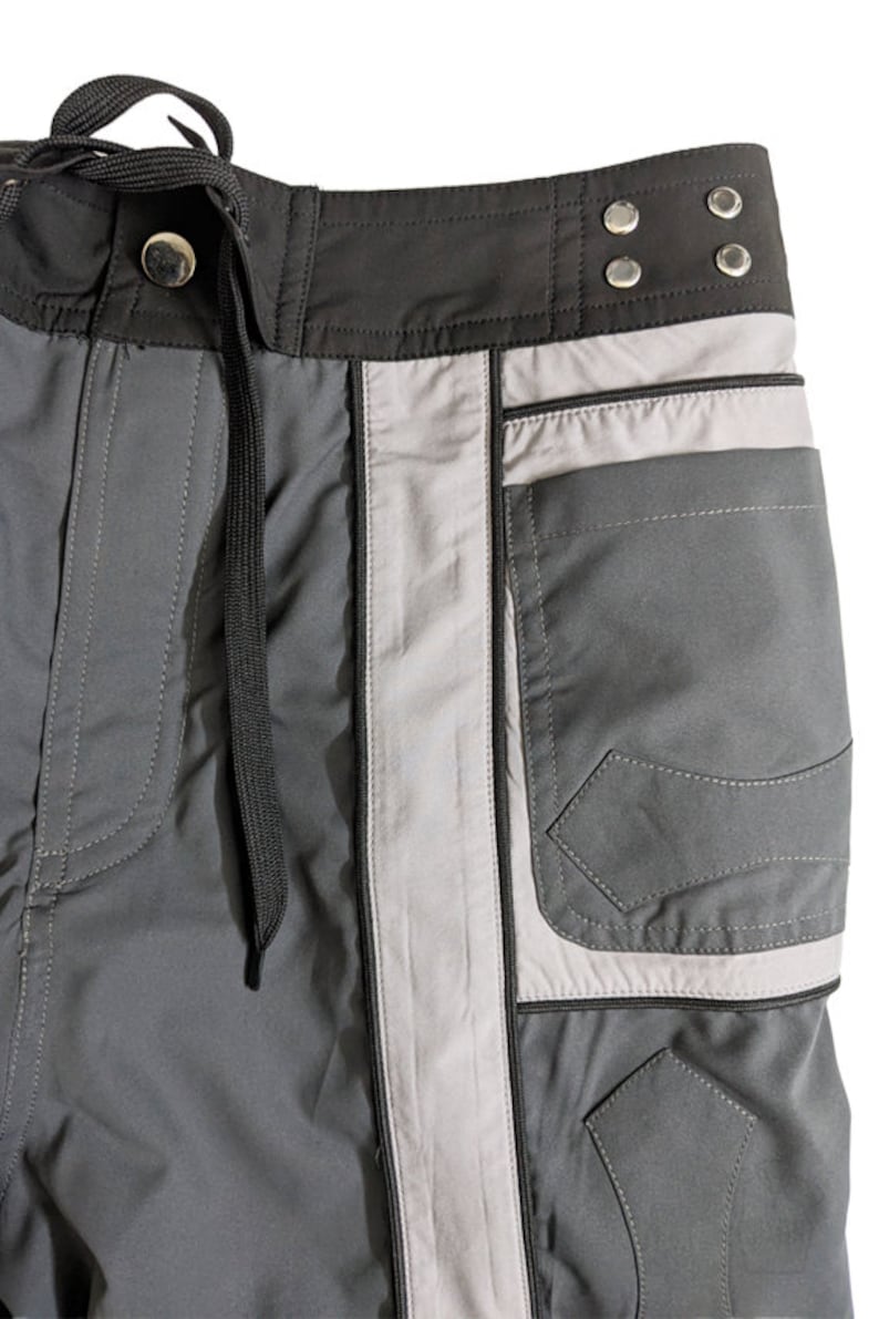 May include: Gray cargo shorts with a black waistband and a silver stripe down the side. The shorts have a large pocket on the right side.