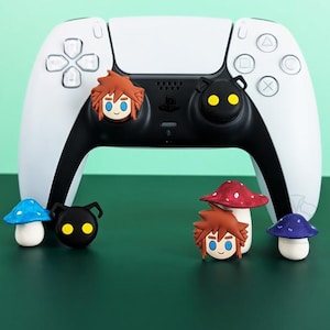 May include: A white and black game controller with character-themed accessories. The accessories include mushroom and character designs in various colors. The controller is on a green surface.