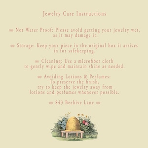 May include: A cream-colored card with jewelry care instructions in red text. The instructions include avoiding water, proper storage, cleaning with a microfiber cloth, and avoiding lotions and perfumes. A decorative illustration of a beehive and flowers is at the bottom.