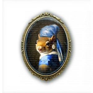 May include: An oval-shaped brooch with a gold-colored frame. The image inside features a squirrel wearing a blue head covering and a pearl earring, reminiscent of a famous painting. The squirrel is wearing a blue top. The background is white.