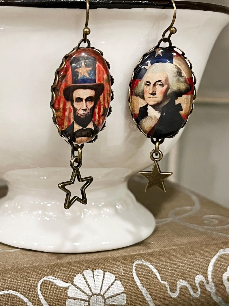 Puede incluir: Pendientes patri&oacute;ticos con colgantes ovalados que representan a Abraham Lincoln y George Washington. Los colgantes est&aacute;n enmarcados con un borde decorativo y tienen colgantes de estrella. Dise&ntilde;o vintage.