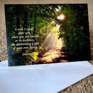 Puede incluir: Una tarjeta de felicitaci&oacute;n con una cita de Hafiz sobre encontrar la luz dentro de ti mismo, con una fotograf&iacute;a de un camino soleado a trav&eacute;s de un bosque.
