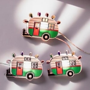 May include: A string of fairy lights with a camper van design. The lights are white and the camper vans are green, white, and red.