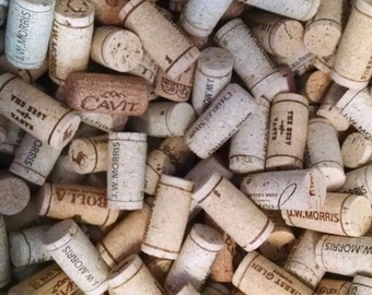 May include: A large collection of cylindrical light brown natural cork wine stoppers piled together. Many of the corks feature printed brand names and text including J.W. Morris, Cavit, Charles Shaw, Forest Glen, and The Best Taste.