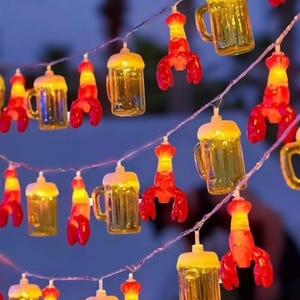 May include: String of lights with clear glass beer mugs and red lobster-shaped lights. The lights are strung together with clear wire.
