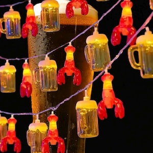 May include: A glass of beer with a string of lights hanging from it. The lights are shaped like beer mugs and lobsters.