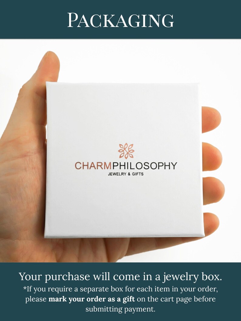A hand holding a white jewelry box with the text "CHARMPhilosophy JEWELRY & GIFTS" printed on it.