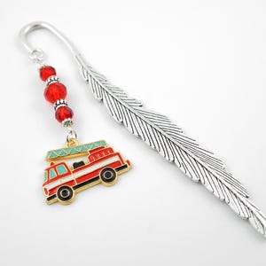 May include: A silver feather bookmark with a red, white, and black fire engine charm. The charm is accented with red beads and a silver hook. A unique accessory for book lovers.