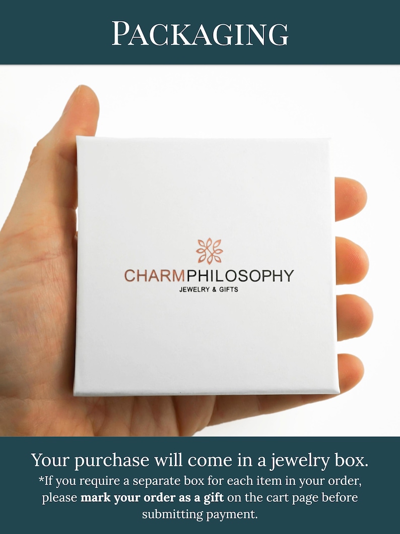 A hand holding a white jewelry box with the text "CHARMPhilosophy JEWELRY & GIFTS" printed on it.
