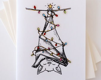 May include: A black and white illustration of a bat hanging upside down with colorful Christmas lights wrapped around it. The bat has a star on its head and is surrounded by a white background.