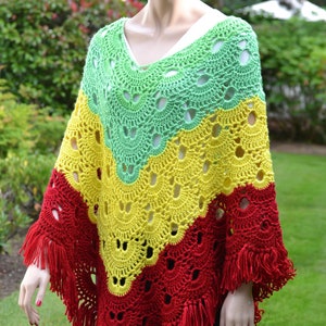 Puede incluir: Un poncho de ganchillo con un esquema de color verde, amarillo y rojo. El poncho tiene un borde de flecos y un cuello en V.