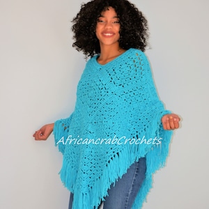 Puede incluir: Un poncho de crochet azul turquesa con flecos. El poncho lo lleva una persona con el pelo rizado y unos vaqueros azules. El texto "AfricancrabCrochets" es visible en el poncho.