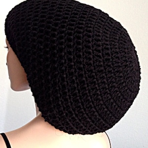 May include: A black crocheted beanie hat with a rounded shape. The hat is made with a simple stitch pattern and has a soft, textured look.