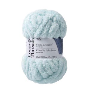 Op de afbeelding: Een bol lichtblauw Loops & Threads Fluffy Chenille polyestergaren. Het etiket geeft 21 m / 300g aan. Het garen heeft een zachte, donzige textuur, ideaal voor brei- en haakprojecten.