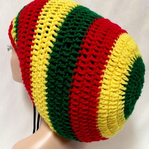 Puede incluir: Un gorro de punto de ganchillo en rayas rojas, amarillas y verdes. El gorro tiene un ajuste holgado y desgarbado y está hecho con un punto de ganchillo simple.