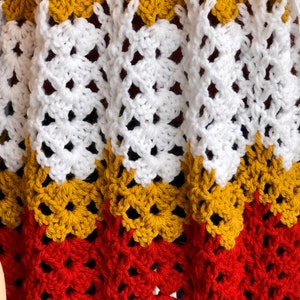 May include: A crocheted blanket with a repeating pattern of red, yellow, and white squares.