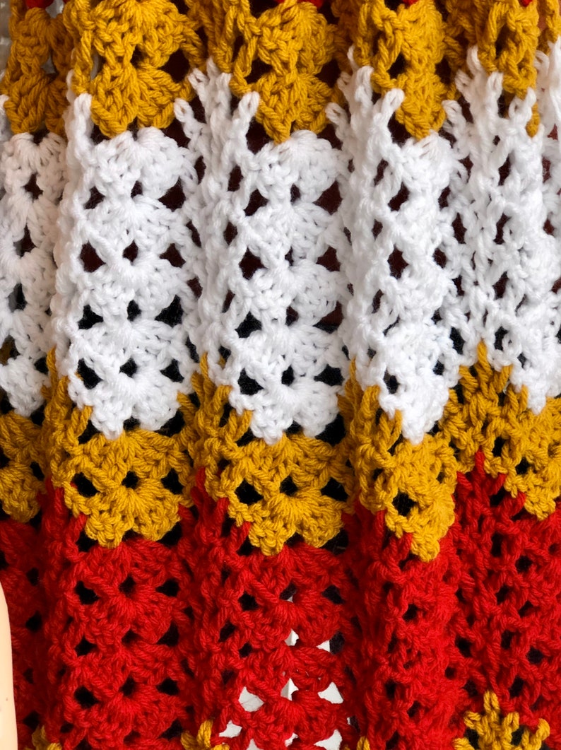 May include: A crocheted blanket with a repeating pattern of red, yellow, and white squares.