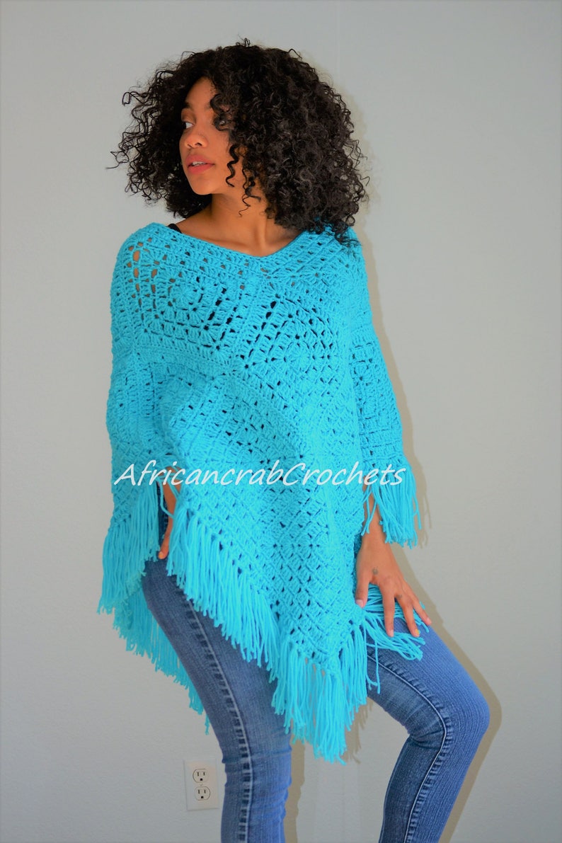 Puede incluir: Un poncho de crochet turquesa con flecos. El poncho lo lleva puesto una persona con el pelo rizado. El texto "AfricancrabCrochets" es visible en el poncho.