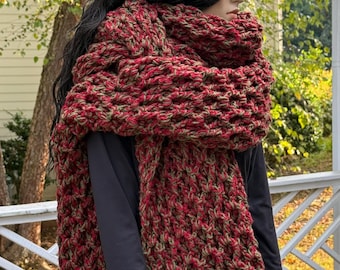 Könnte beinhalten: Ein grober, handgestrickter Schal aus einer Mischung aus roter und olivgrüner Wolle. Der Schal ist um eine Schaufensterpuppe gewickelt und zeigt sein dickes, strukturiertes Gewebe. Ein gemütliches Accessoire.