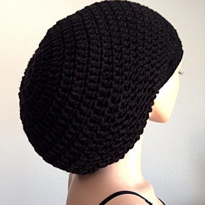 May include: A black, crocheted beanie hat. The hat is made of a thick yarn, with a textured, ribbed pattern. The hat is shown on a mannequin head, and the background is a plain white wall.