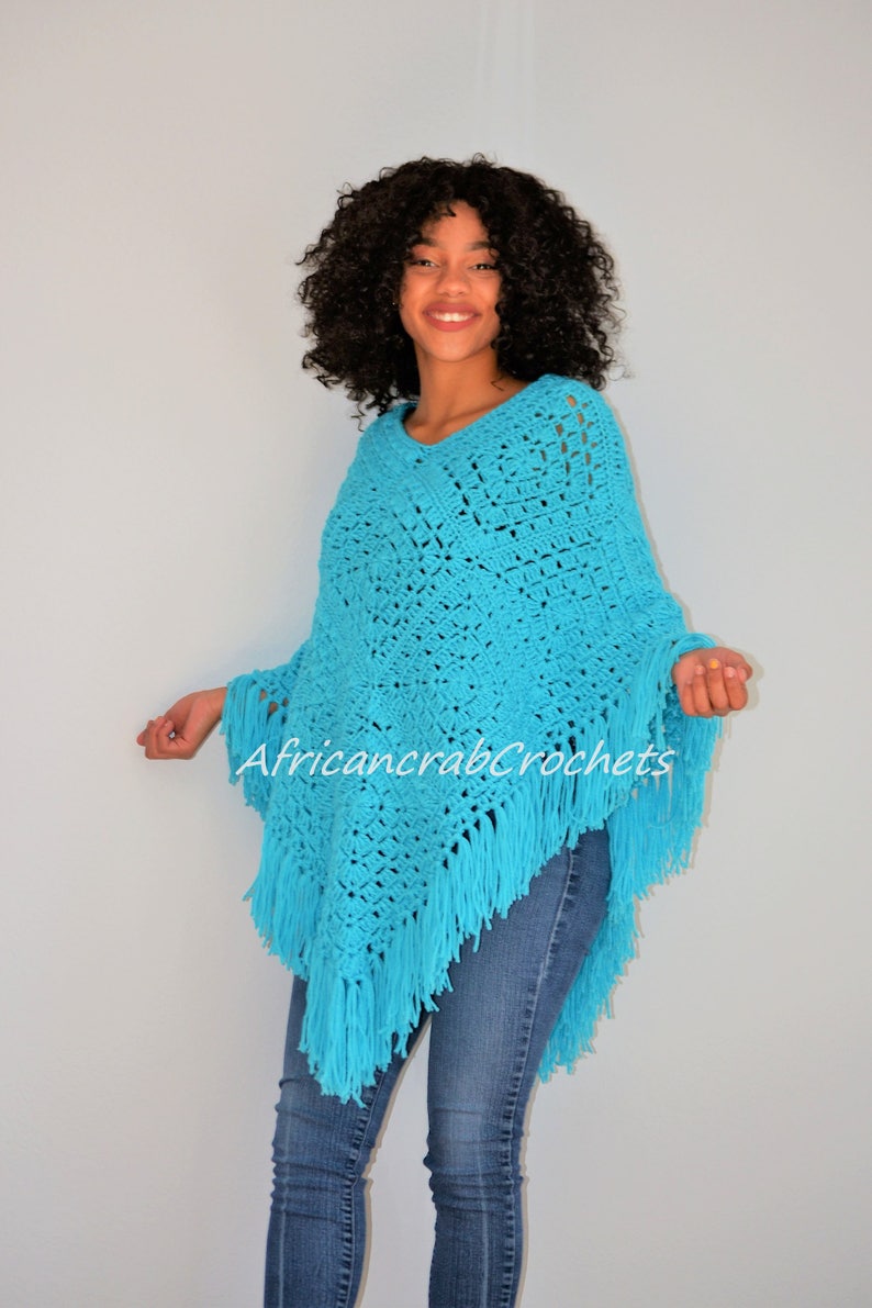 Puede incluir: Un poncho de crochet azul turquesa con flecos. El poncho lo lleva una persona con el pelo rizado y unos vaqueros azules. El texto "AfricancrabCrochets" es visible en el poncho.