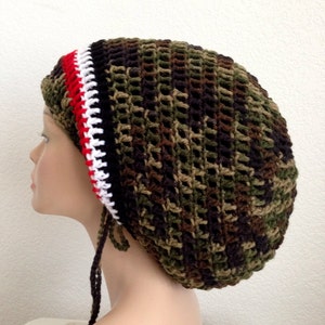 May include: A green, brown, and black camouflage crochet beanie with a red, white, and black trim. The beanie has a long black string tie.