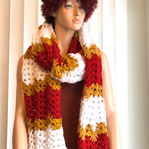 May include: A crocheted scarf in red, white, and gold stripes. The scarf is made with a lacy stitch and is long enough to be worn as a wrap.