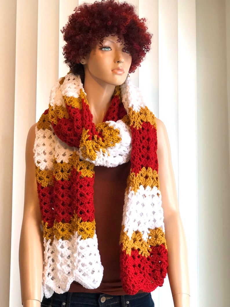 May include: A crocheted scarf in red, white, and gold stripes. The scarf is made with a lacy stitch and is long enough to be worn as a wrap.