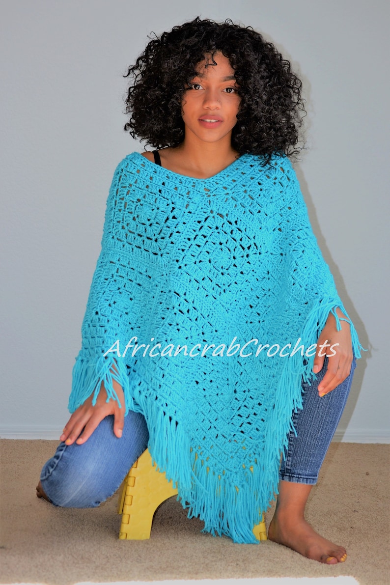 Puede incluir: Un poncho de crochet turquesa con flecos. El poncho est&aacute; hecho con un patr&oacute;n de punto cuadrado. La modelo lleva el poncho y est&aacute; sentada en un taburete amarillo.