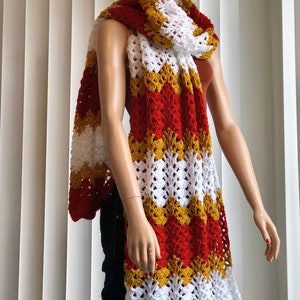 May include: A long, crocheted scarf with red, white, and gold stripes. The scarf is made with a lacy stitch and has a scalloped edge.