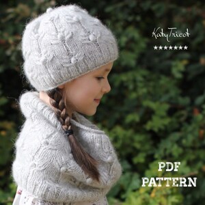May include: A light gray knitted hat and cowl set with a textured floral pattern. The hat is a close-fitting style, and the cowl is worn around the neck. The text "Katy Tricot" and "PDF PATTERN" are visible.