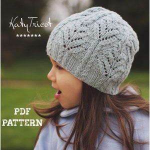May include: A young person wearing a light blue knitted hat with a cable and lace pattern. The hat is labeled "Katy Tricot" and "PDF PATTERN".