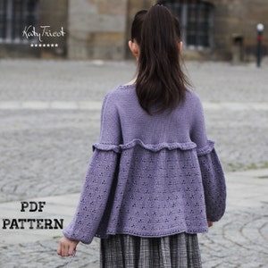 May include: A purple knitted sweater with a lacy pattern and a ruffled hem. The sweater has long sleeves and a loose fit. The text "PDF PATTERN" is visible in the bottom left corner of the image.