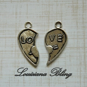 May include: Two silver charm pendants shaped like broken hearts. One heart says "LOVE" and the other says "LO".